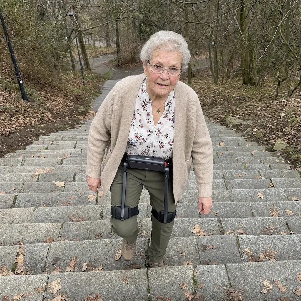 Egzoszkielet a schody — w górę i w dół to dwa różne zadania Kobieta w egzoszkielecie WIM S wchodzi po kamiennych schodach w parku